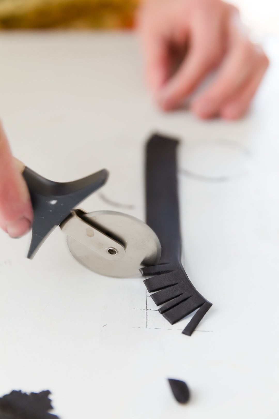 Using a pizza cutter to cut fringes into rolled black fondant