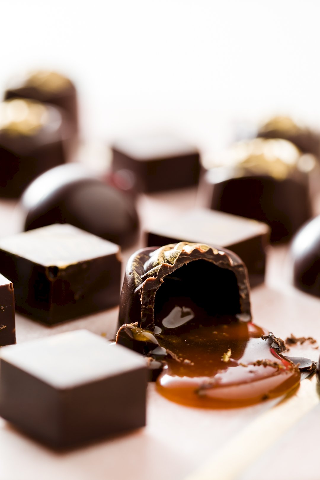 An assortment of bonbons with one cut open and spilling caramel out all over a marble slab