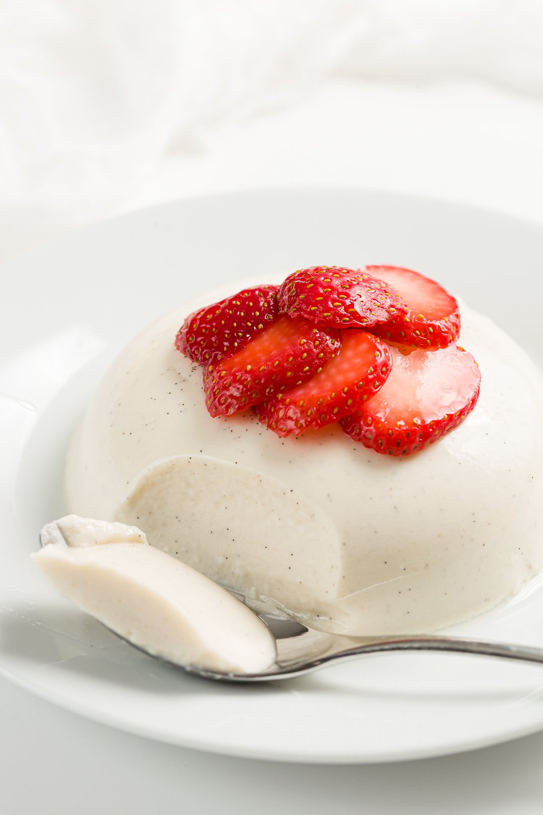 panna cotta on a plate served with macerated strawberries with a spoonful removed