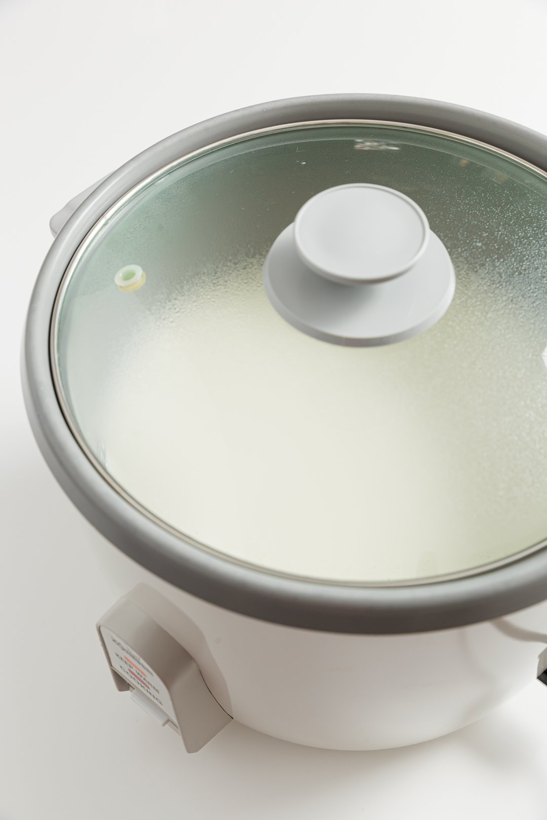 A lidded rice cooker filled with heavy whipping cream on its keep warm setting