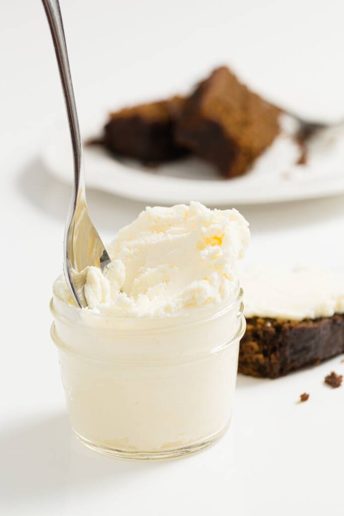  Une cuillère reposant dans un bocal rempli de crème coagulée avec des desserts derrière elle