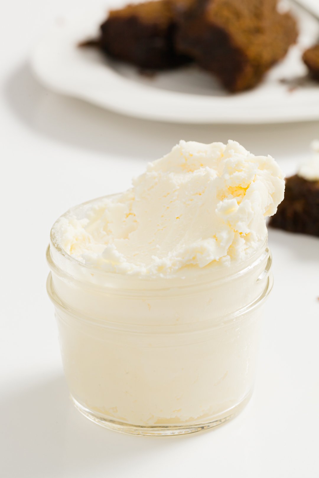 A jar of clotted cream in the foreground with desserts in the background