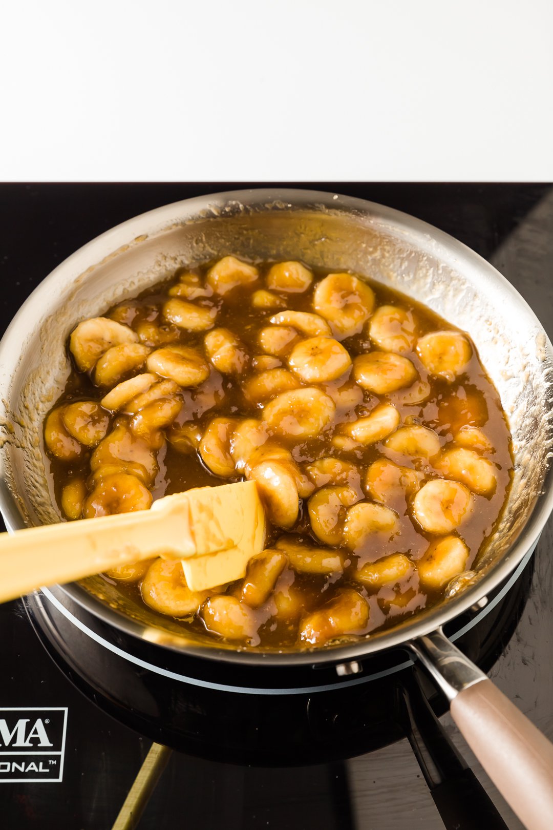 Caramelized bananas in a skillet with a yellow spatula
