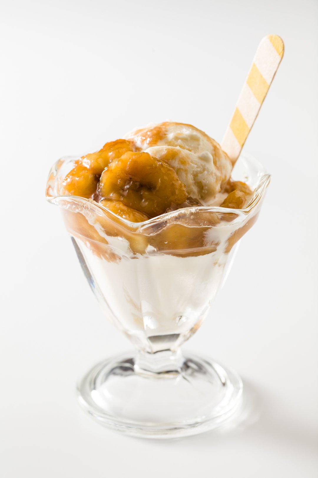 Caramelized bananas over vanilla ice cream in a glass dish with a spoon