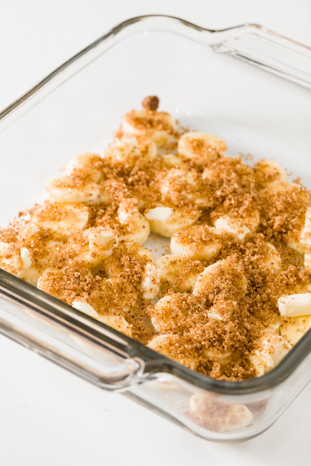 Bananas slices in a glass baking dish topped with butter and brown sugar