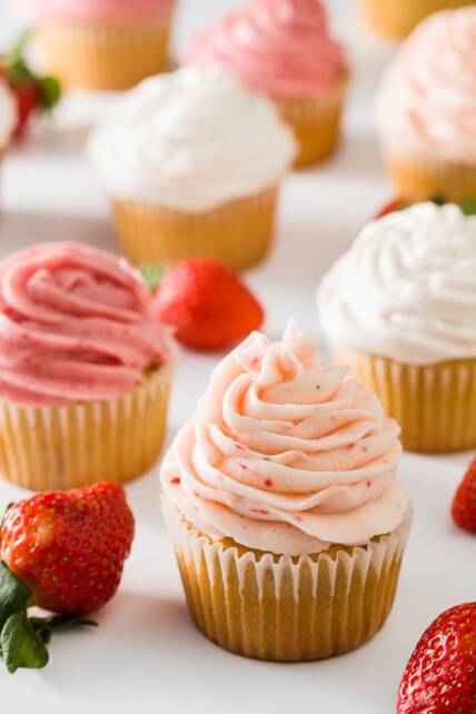 Cupcakes glaseados con tres tipos de glaseado de fresa sobre un fondo blanco con algunas fresas dispersas