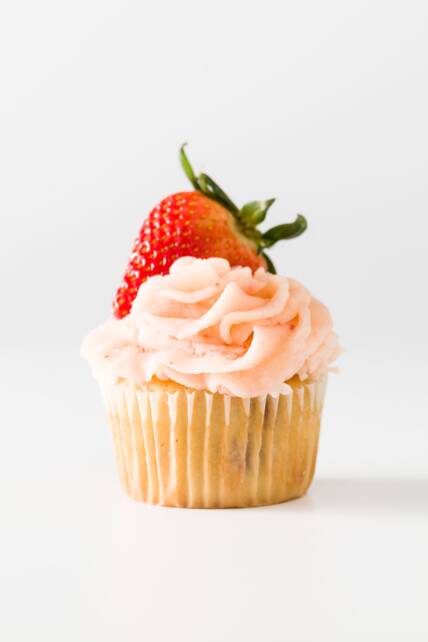 Un cupcake de fresa con glaseado de crema de mantequilla de fresa y una fresa en la parte superior