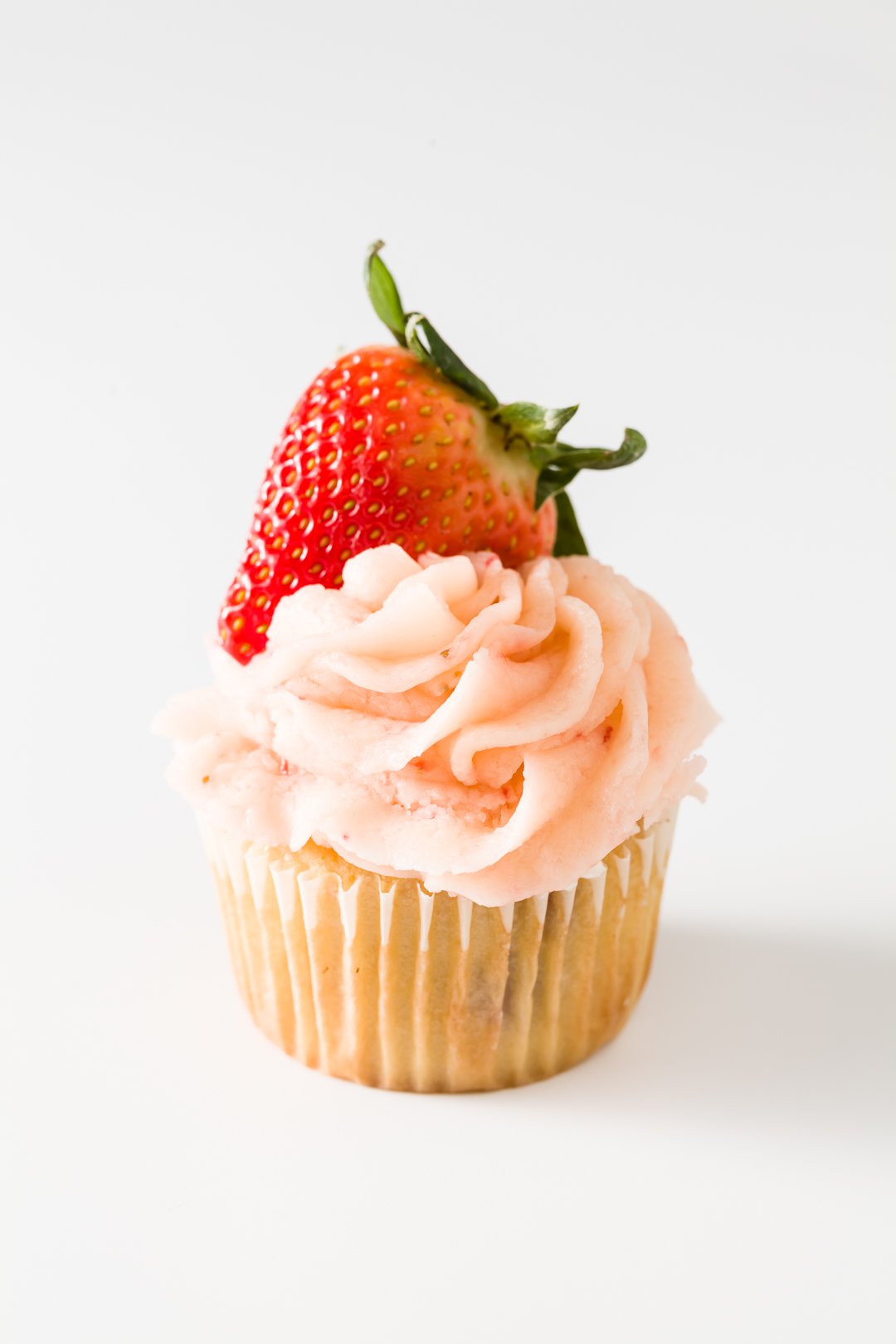 a cupcake frosted with strawberry buttercream frosting and topped with a strawberry
