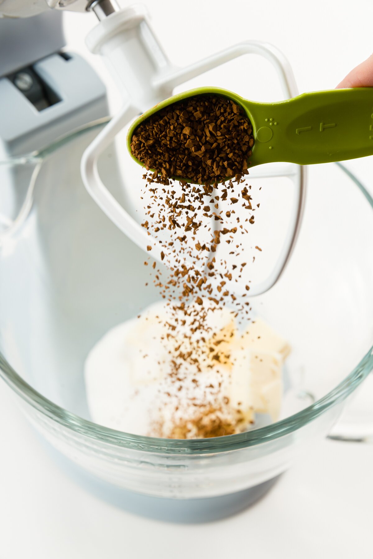 Pouring instant coffee into a stand mixer with butter and sugar
