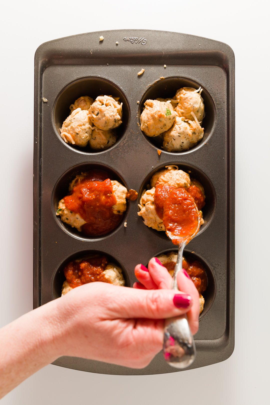 Filling muffin tins with pizza dough and sauce
