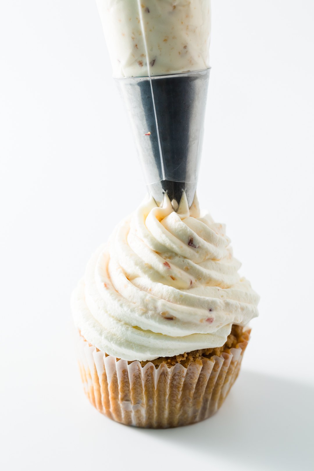 Peach whipped cream being piped onto a cupcake