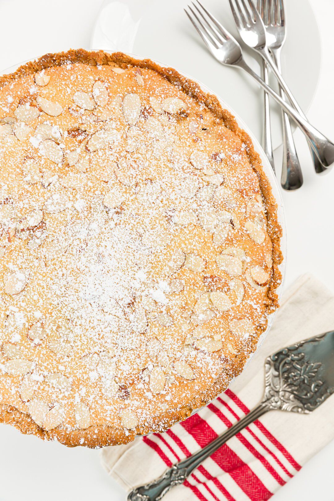 overhead shot of cooked tart dusted with powdered sugar with a cake server next to it on a striped napkin