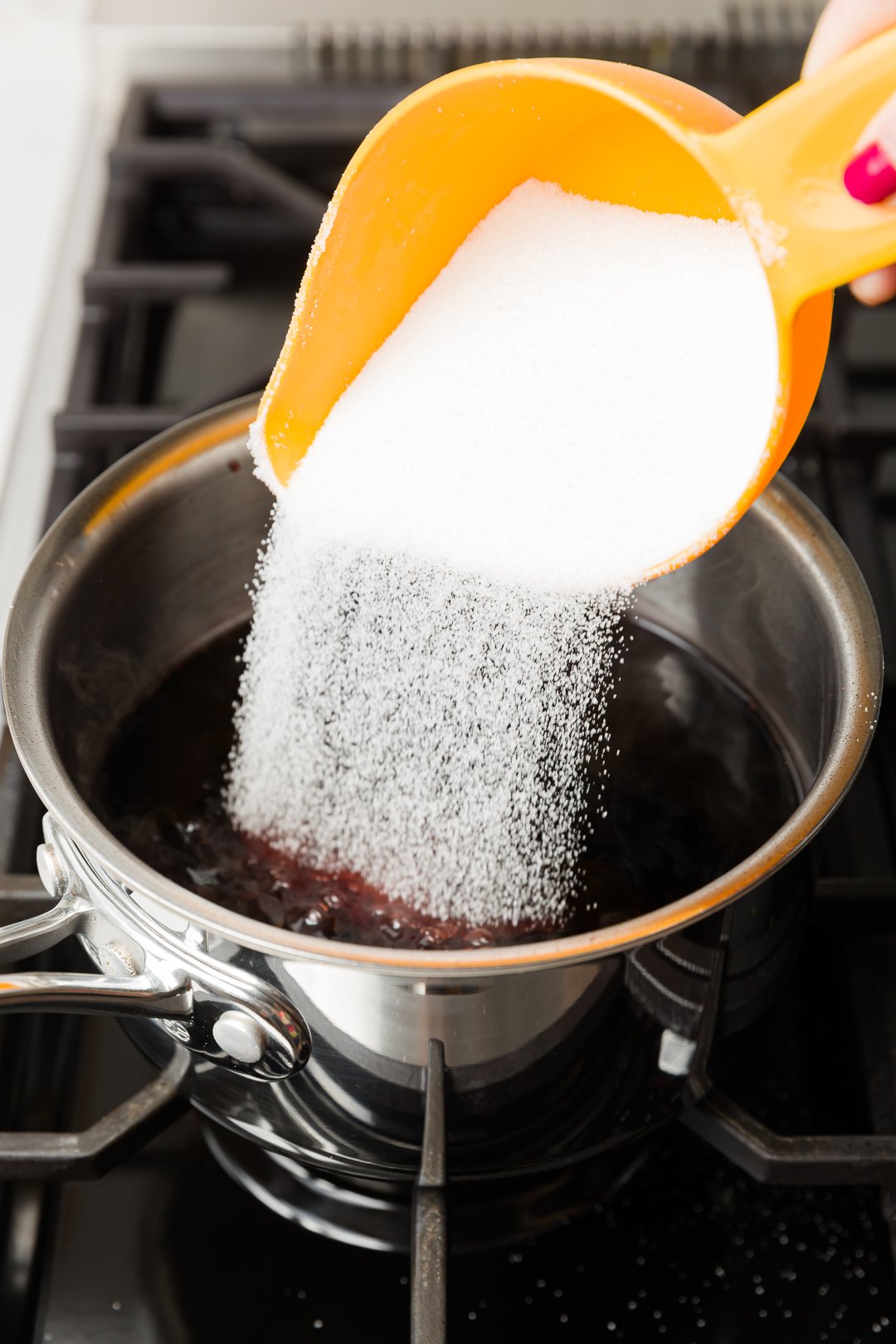 sugar poured into pomegranate juice, slowly boiling in a pot on a range, to make grenadine