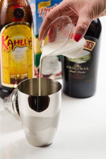 crema espesa agregada a una coctelera con hielo para hacer un cóctel de deslizamiento de tierra