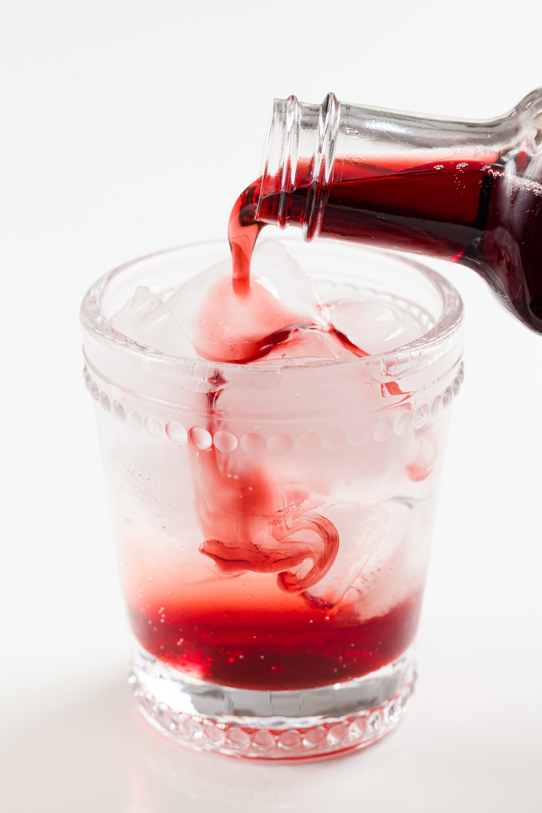 pouring homemade grenadine into a glass of lemon-lime soda in order to make a Shirley Temple non-alcoholic cocktail