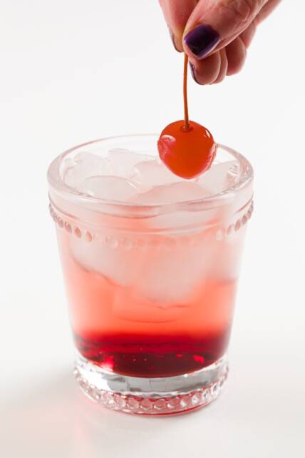 colocando una cereza marrasquino en un cóctel sin alcohol de Shirley Temple
