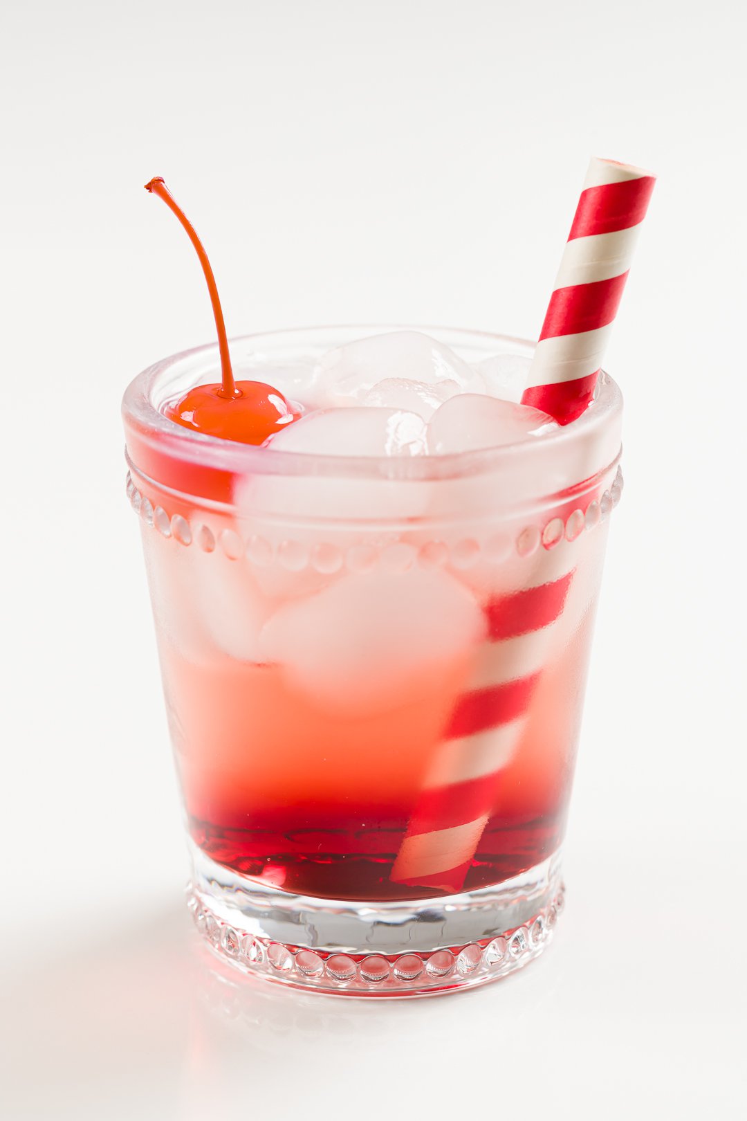 A glass with a Shirley Temple non-alcoholic cocktail, Maraschino cherry, and straw