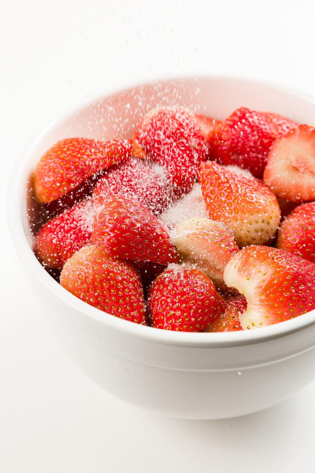 Sugar being poured over a large bowl of strawberries