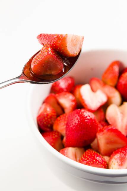 Fresas maceradas en una cuchara flotando sobre un tazón grande lleno de fresas maceradas