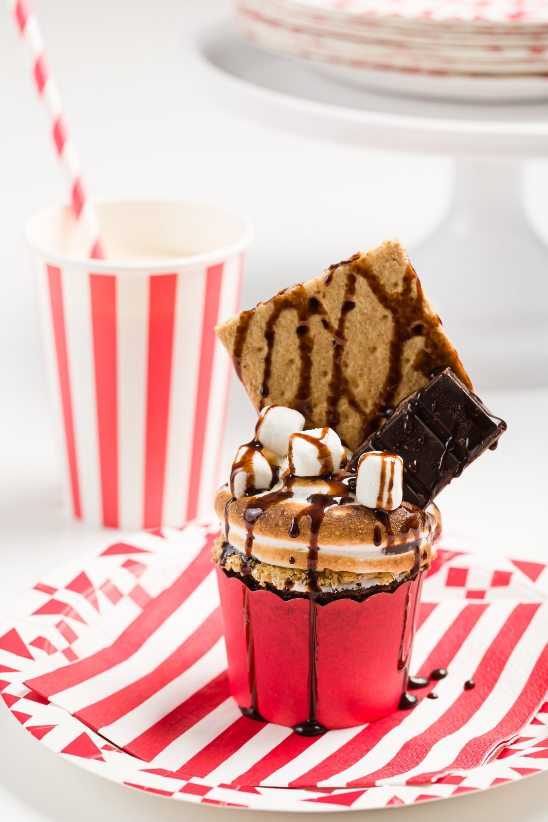 S'mores cupcake party on a red and white striped plate with a matching cup and straw in the background