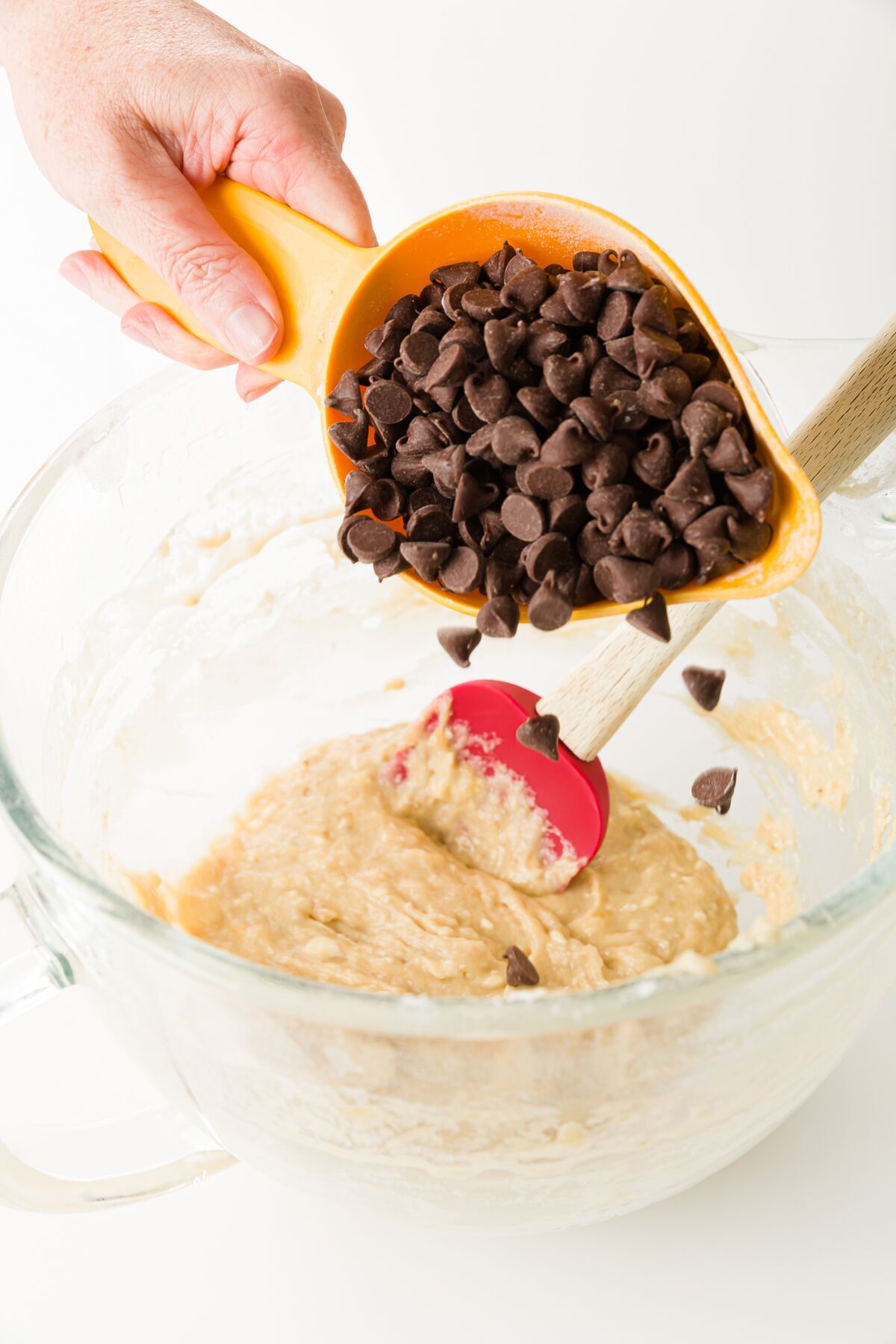A cup of chocolate chips being poured into a glass mixing bowl
