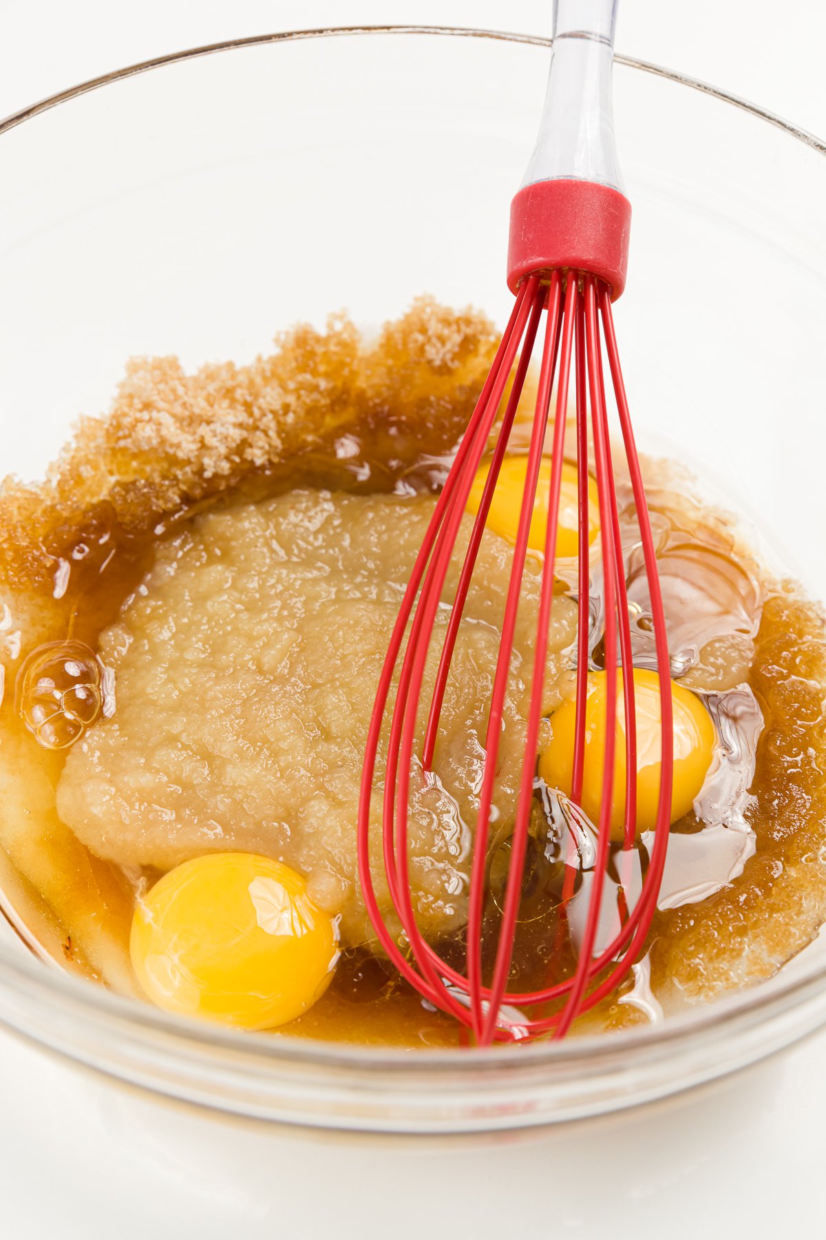 Red whisk whisking eggs and other ingredients in a glass bowl