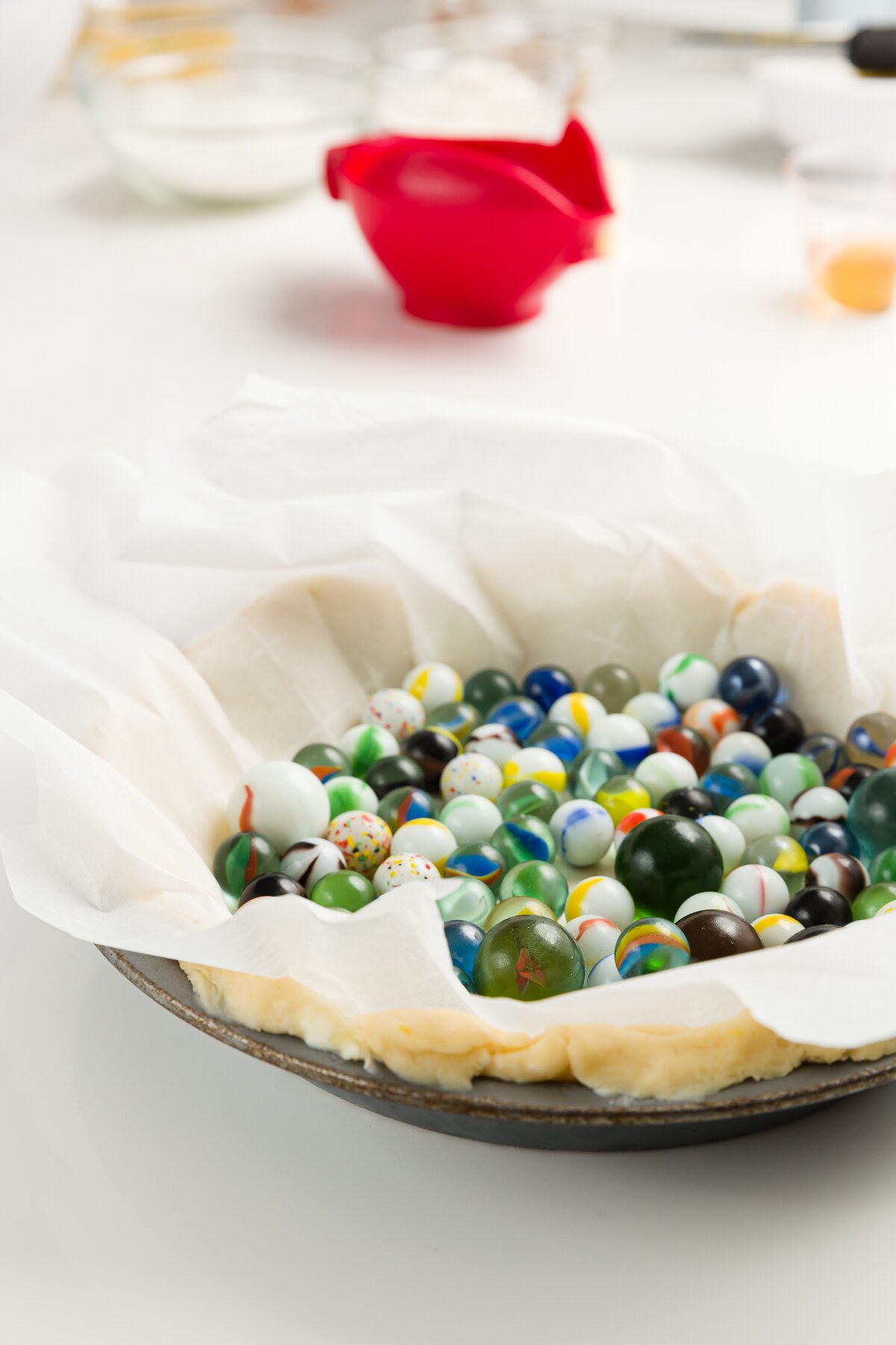 pie pan with pie crust in it, topped with parchment paper and lots of marbles