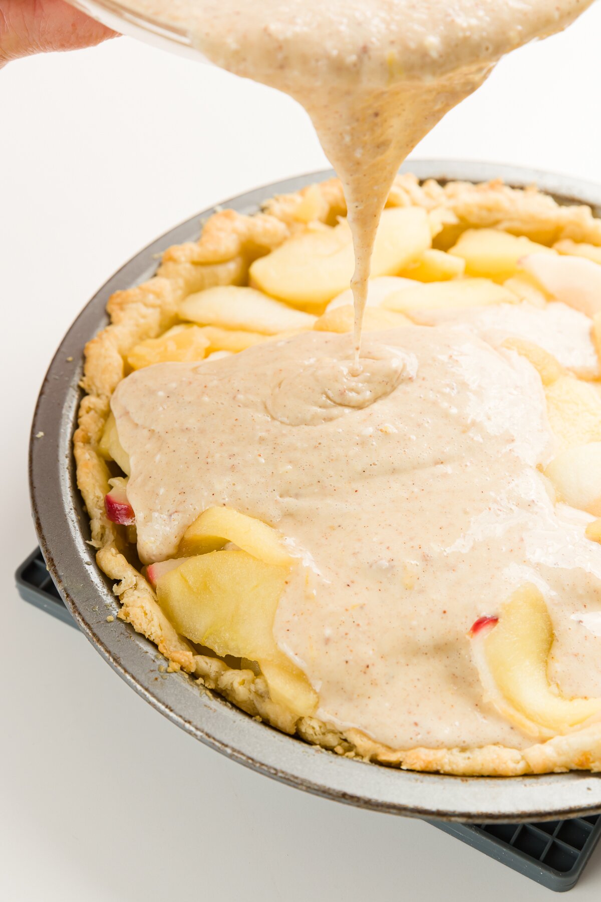 Pouring custard over apples in a pie pan