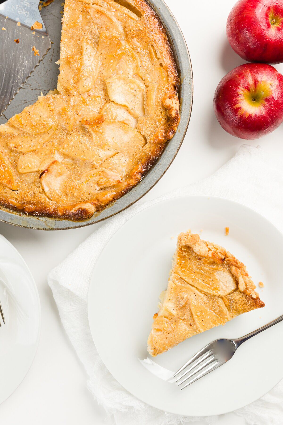 Apple custard pie in a pan with a slice cut out and an apple next to it