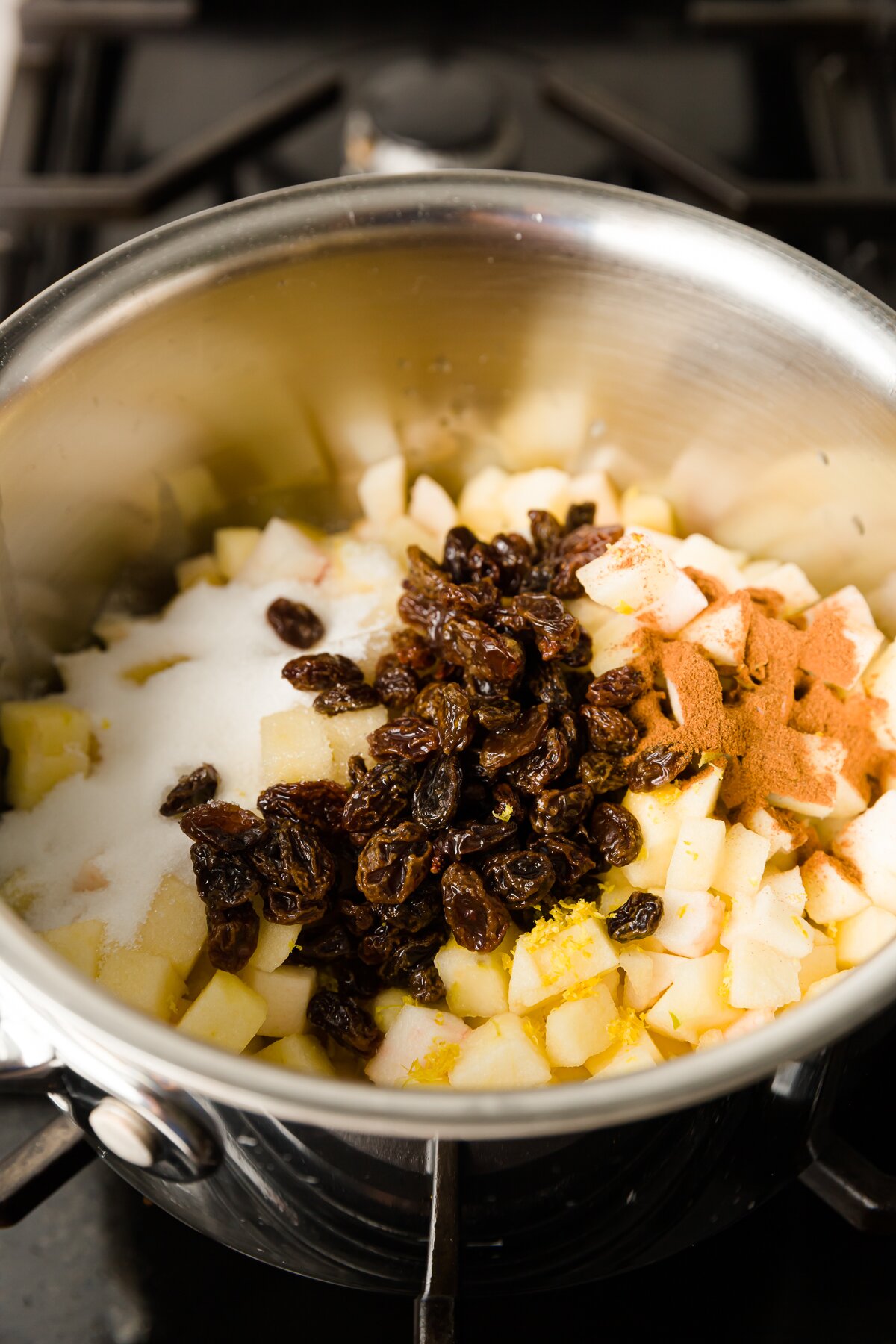 Pot with diced apples, cinnamon, sugar, and dark raisins on the stove