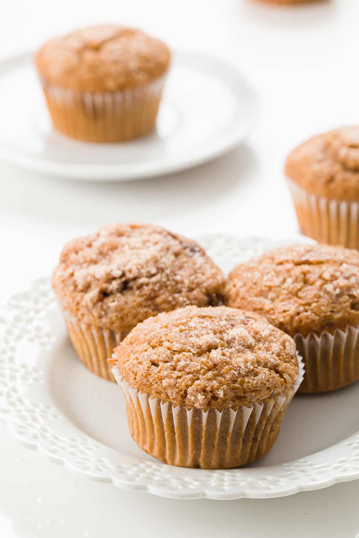 Three cinnamon muffins on a white plate with a muffin in the background