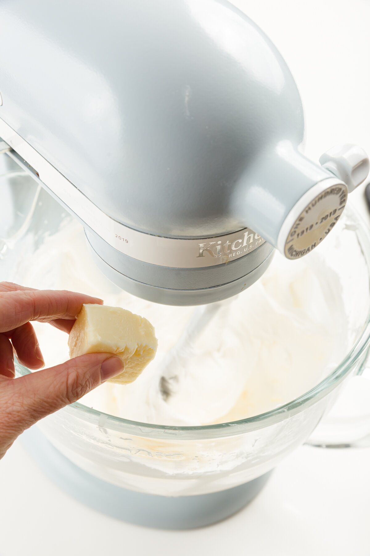 tight shot of Stef adding butter to a mixer full of Italian meringue buttercream frosting