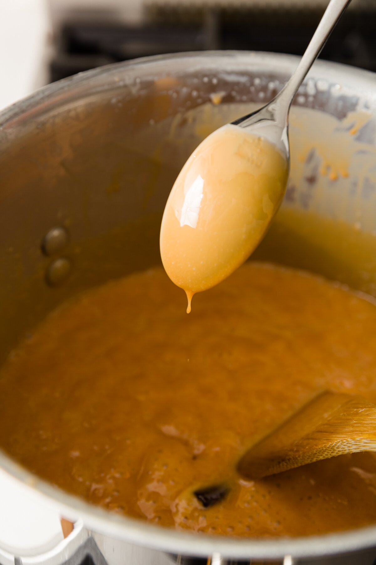 view of a spoon with cajeta sticking to it hovering over a pot of boiling cajeta