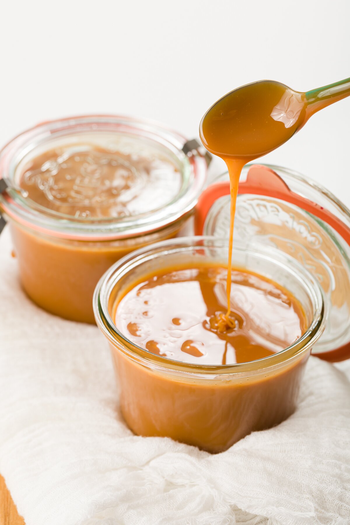 two jars of cajeta with a spoon full of the caramel drizzling its contents back into the jar