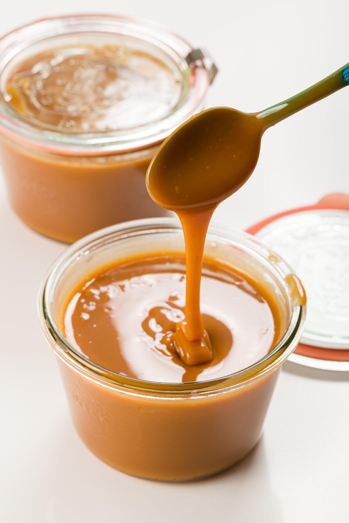 two jars of cajeta with a spoon full of the caramel drizzling back into one