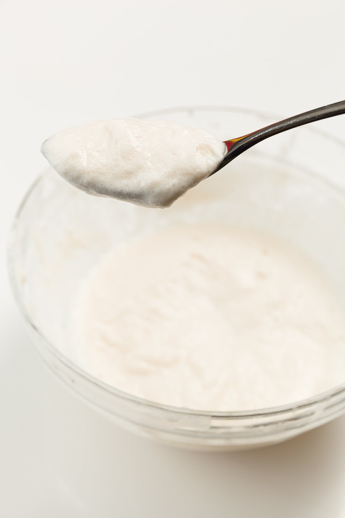 a spoon containing froth from a syllabub cocktail held above a bowl with the drink