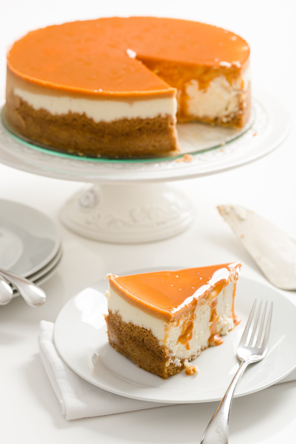 Slice of dulce de leche cheesecake with the full cake on a cake stand behind it