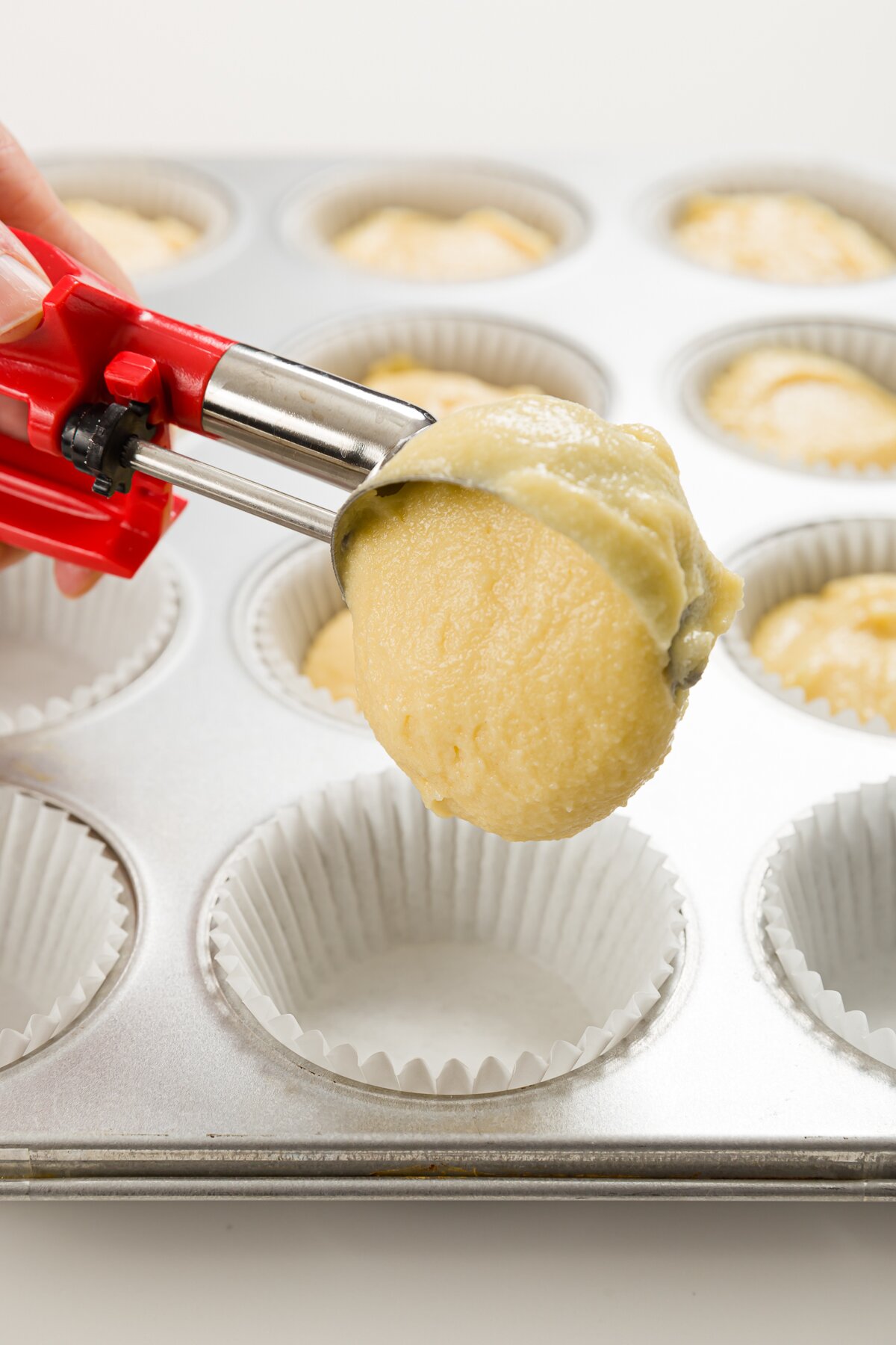 Stef using a disher to fill a cupcake liner with pound cake cupcake batter