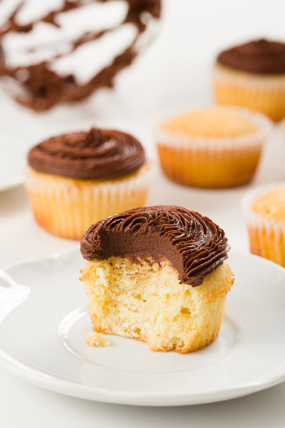 view of an interior of a pound cake cupcake frosted with chocolate ganache frosting with other cupcakes in the background