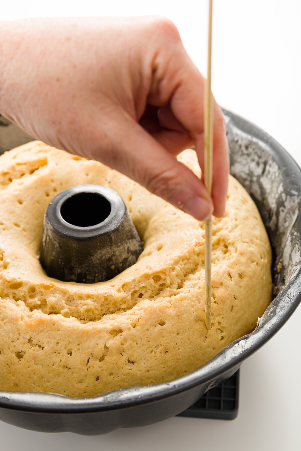 medium shot of Stef poking holes into the cake still in the Bundt pan using a skewer
