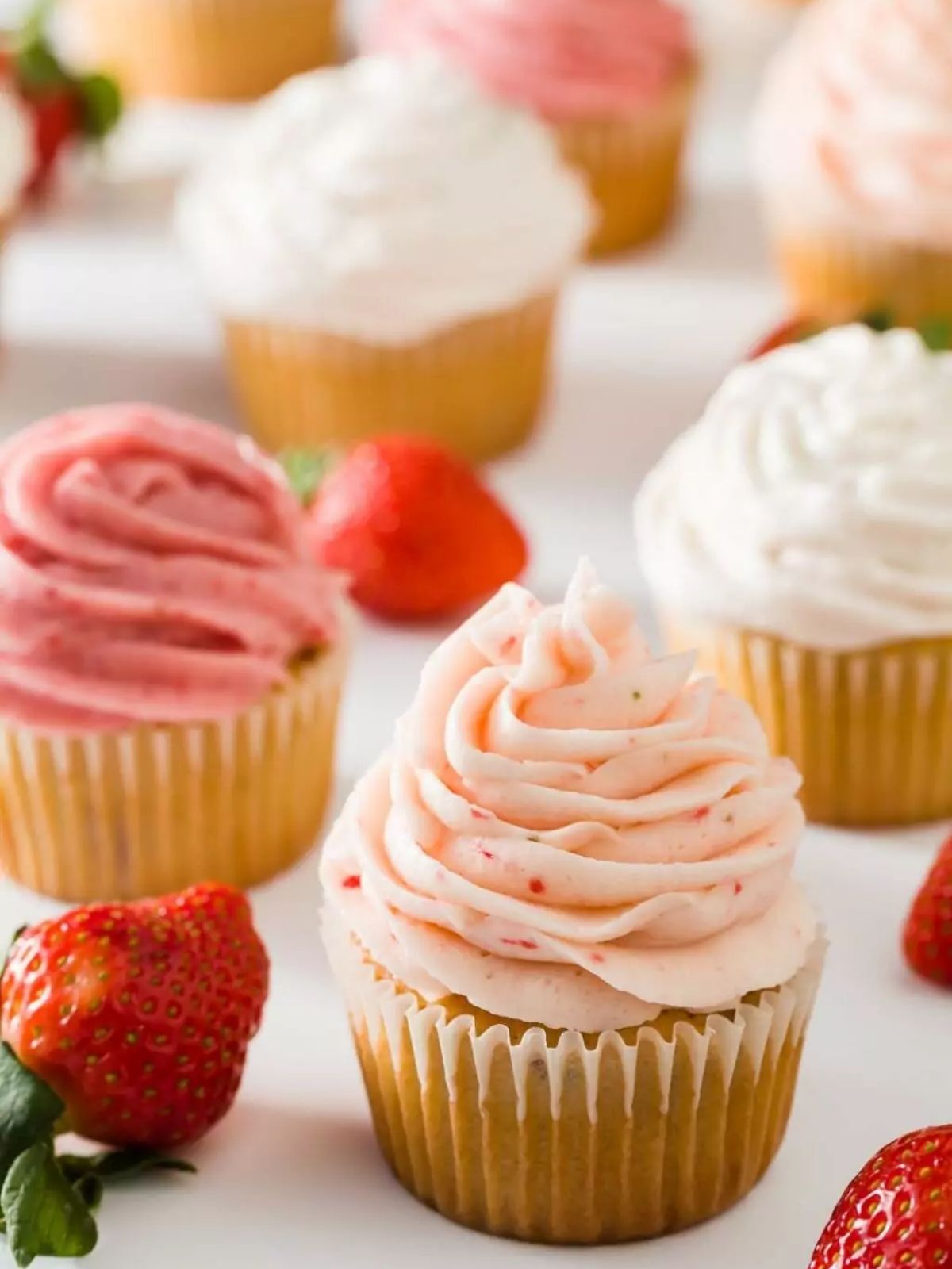 Strawberry cupcakes with strawberry buttercream frosting and fresh strawberries around them.