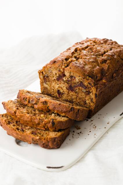 Date nut bread on a white serving plate, partially sliced