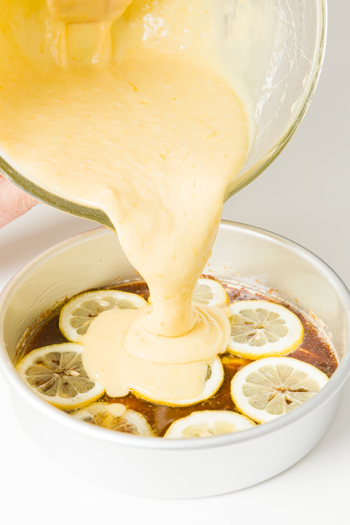 Pouring batter over pan with lemons in it