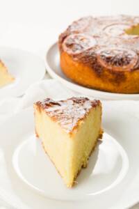 slice of lemon olive oil cake on a plate with the cake in the background