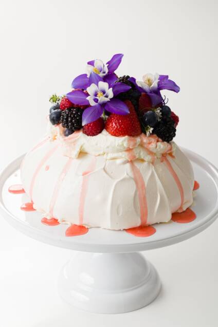 pavlova covered with whipped cream, fresh fruit, and flowers