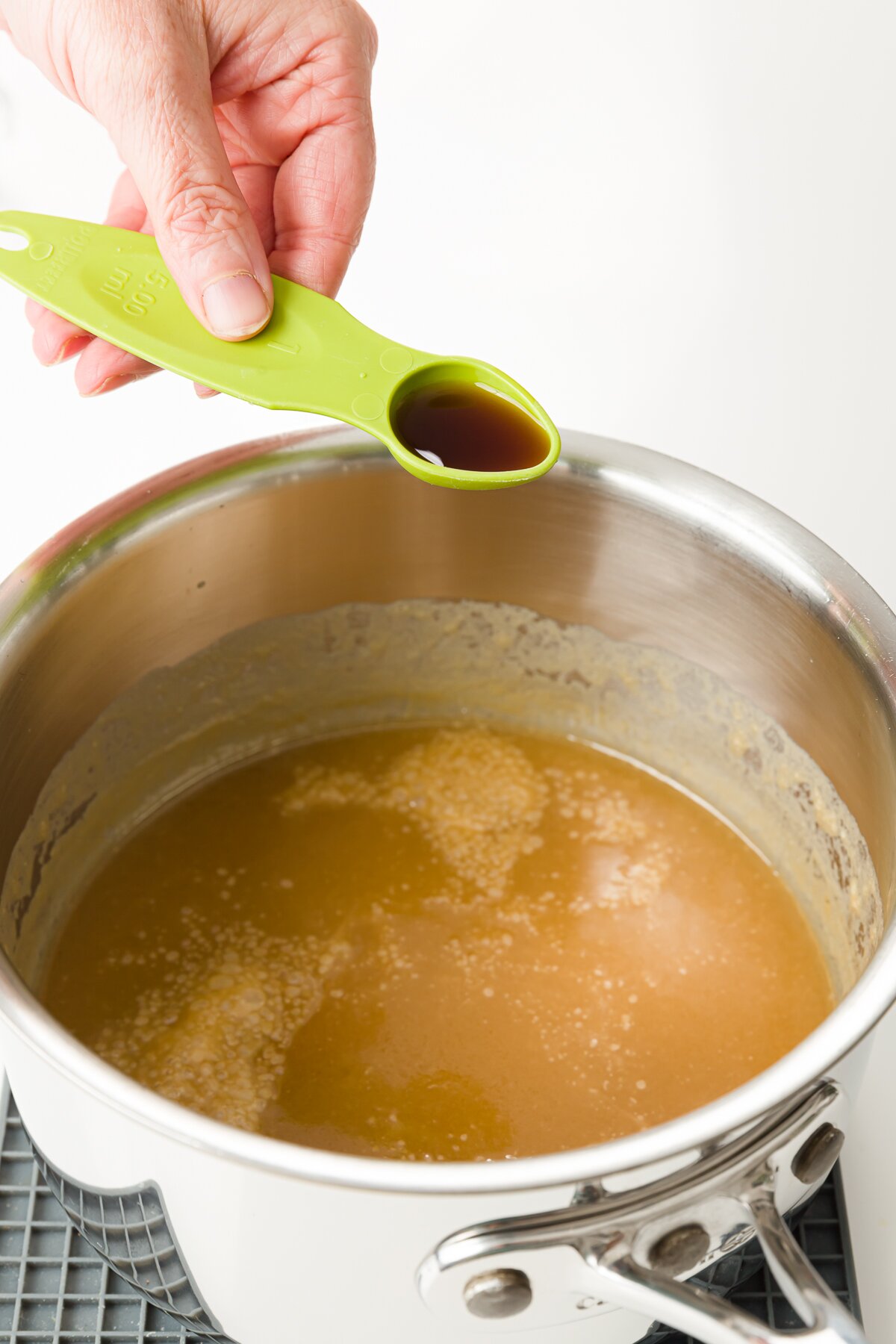 Adding vanilla in a green measuring spoon to pot of butterscotch sauce
