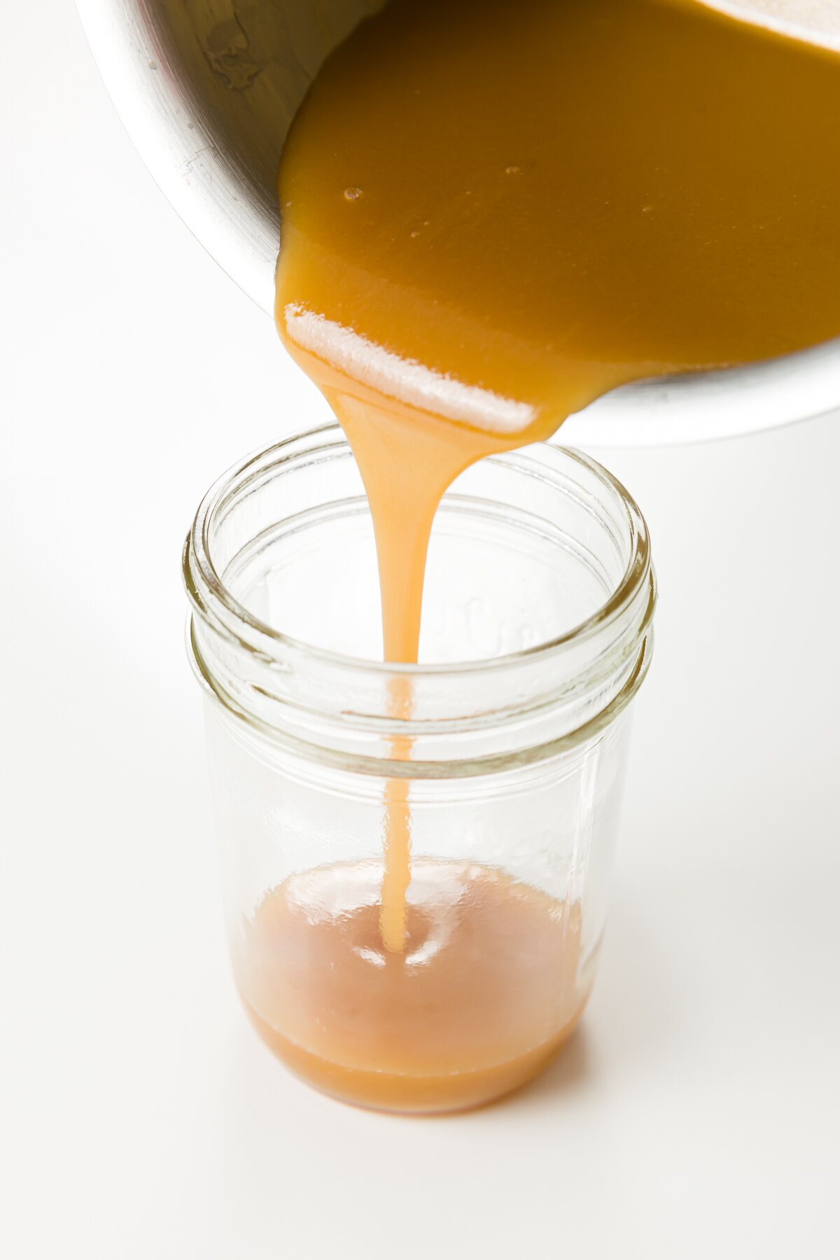 pouring whiskey sauce into a jar from a pot