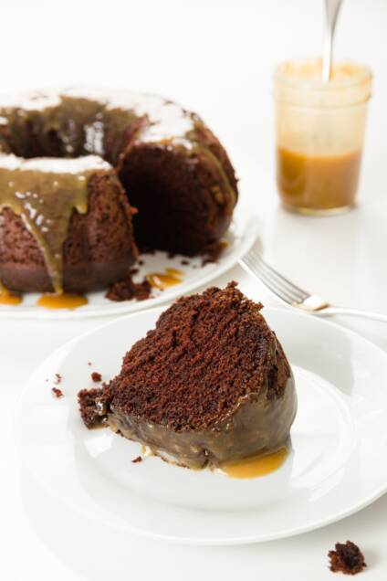 Slice of chocolate whiskey cake with Bundt cake and jar of whiskey sauce in the background