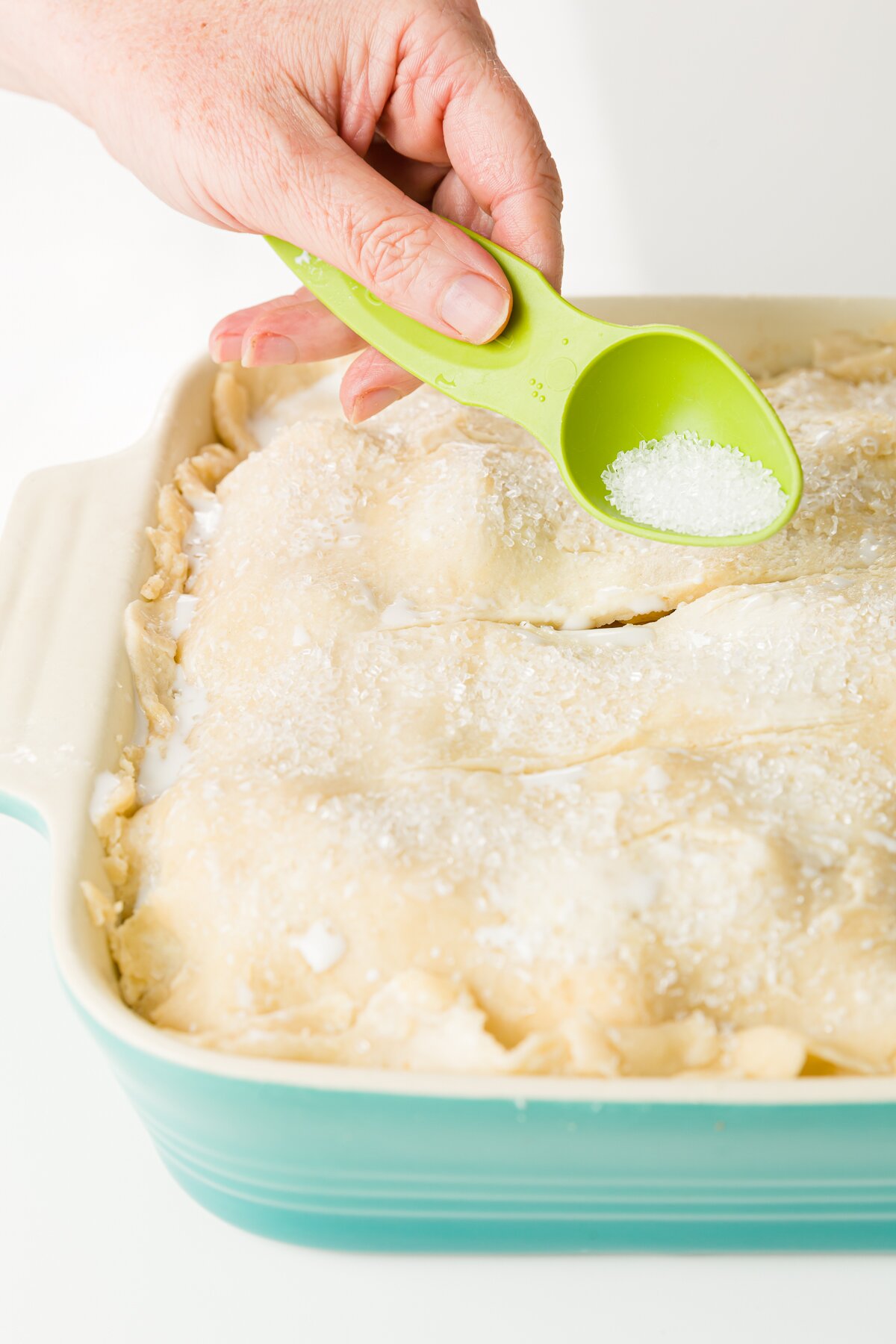 Adding sparkly sugar onto pie crust from a green tablespoon