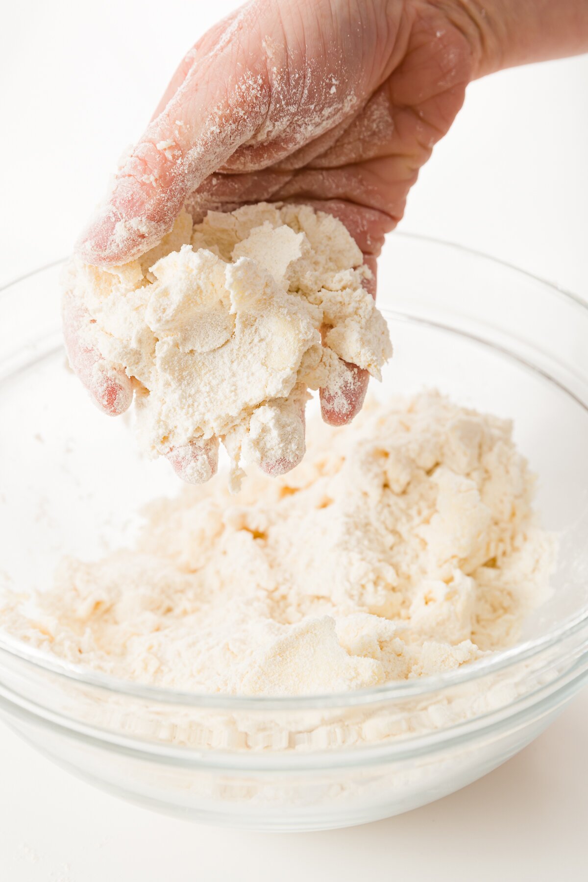 Hand holding a buttery dough over a glass bowl